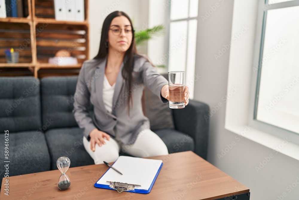 Young beautiful hispanic woman psychologist offering glass of water at psychology clinic Young beautiful hispanic woman psychologist offering glass of water at psychology clinic