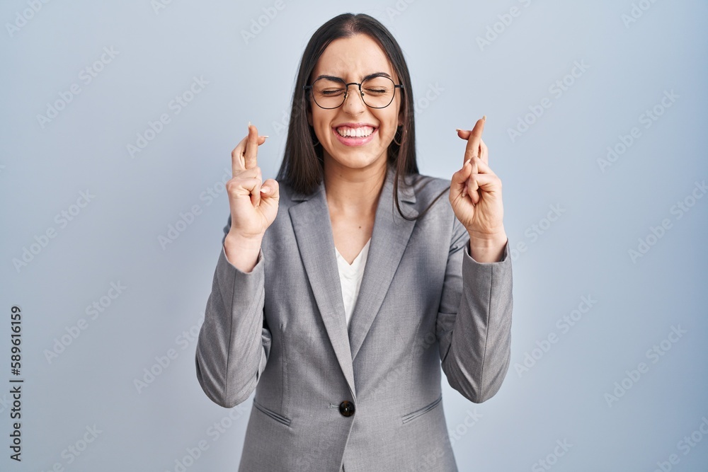Hispanic business woman wearing glasses gesturing finger crossed smiling with hope and eyes closed. luck and superstitious concept. Hispanic business woman wearing glasses gesturing finger crossed smiling with hope and eyes closed. luck and superstitious concept.