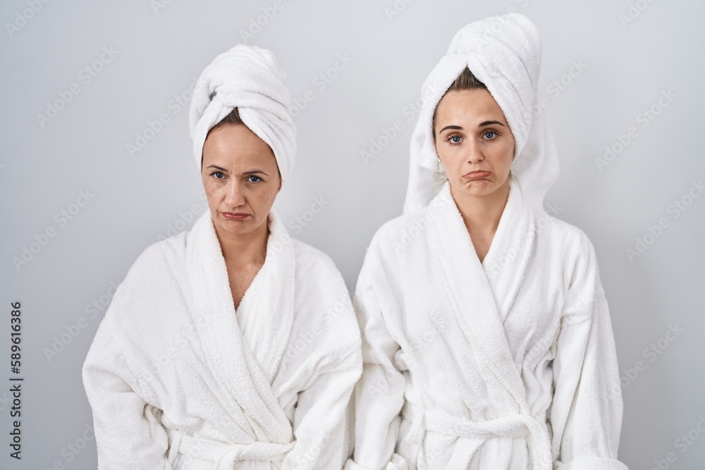 Middle age woman and daughter wearing white bathrobe and towel depressed and worry for distress, crying angry and afraid. sad expression.