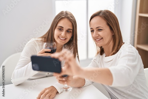 Two women mother and daughter drinking glass of wine make selfie by smartphone at home