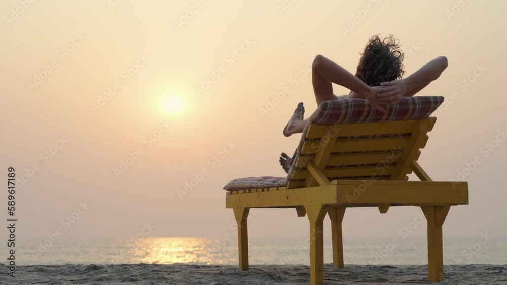 Man at sunset lies on a chaise longue by the sea
