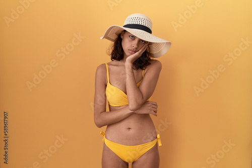 Young hispanic woman wearing bikini and summer hat thinking looking tired and bored with depression problems with crossed arms.