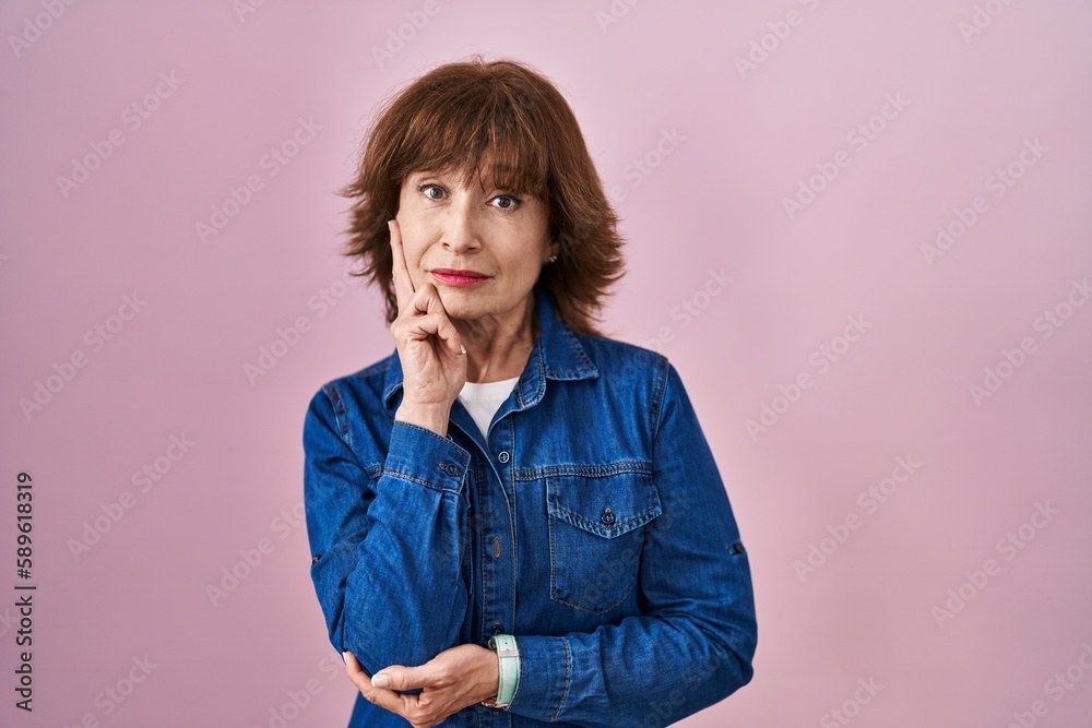 Middle age woman standing over pink background thinking worried about a question, concerned and nervous with hand on chin Middle age woman standing over pink background thinking worried about a question, concerned and nervous with hand on chin