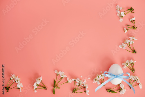 A cherry blossoms and an egg with a blue ribbon on a pink background. Easter background, copy space. Flatlay