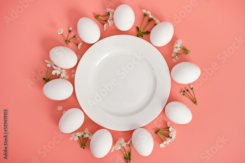 Composition with an empty plate, Easter eggs and beautiful flowers on a pink background, close-up. Space for copying. View from above