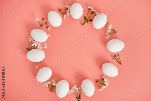 A frame of white flowers and white eggs on a pink background. Copy space, top view. Easter background