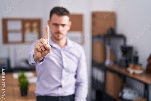 Young hispanic man at the office pointing with finger up and angry expression, showing no gesture