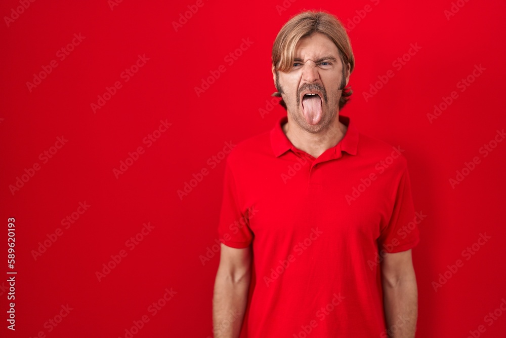 Fototapeta premium Caucasian man with mustache standing over red background sticking tongue out happy with funny expression. emotion concept.
