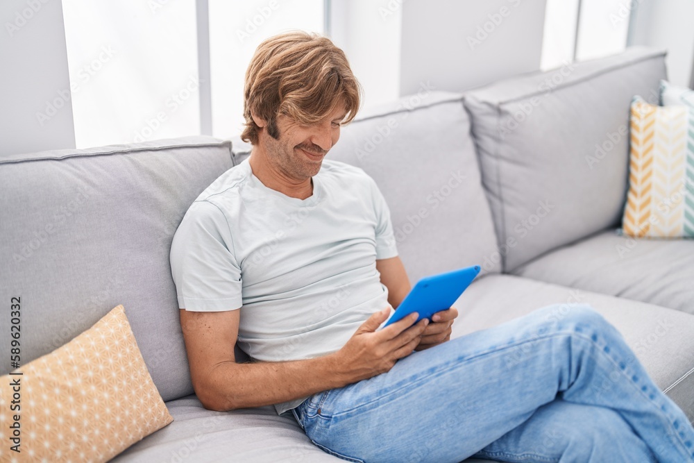 Young man using touchpad sitting on sofa at home