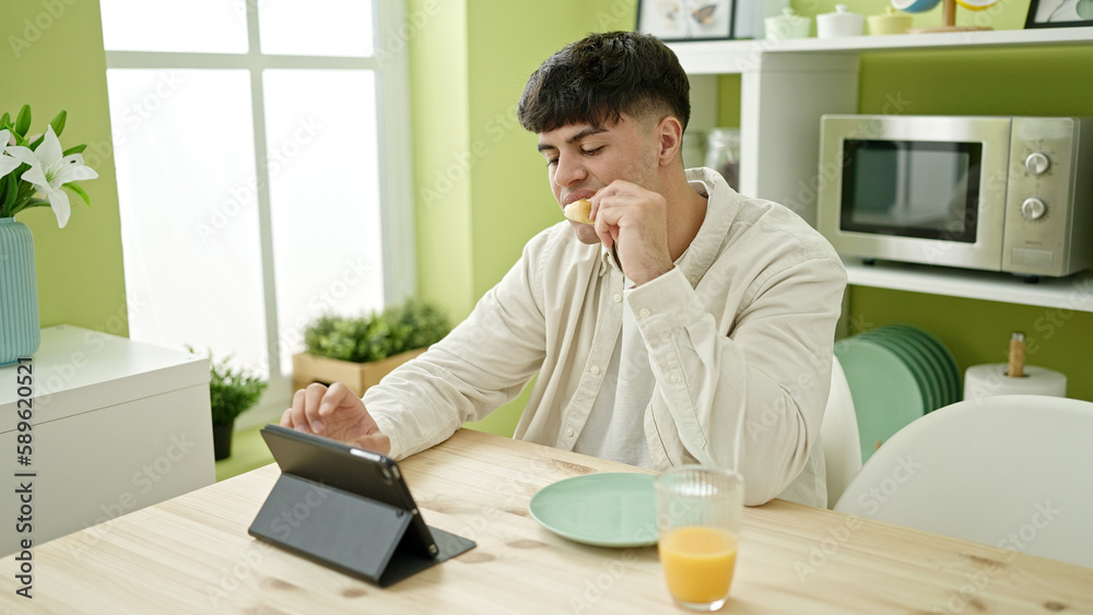 Young hispanic man watching video on touchpad having breakfast at dinning room Young hispanic man watching video on touchpad having breakfast at dinning room