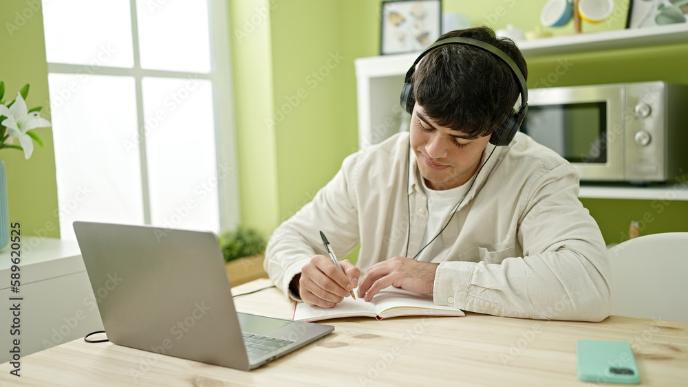 Young hispanic man student using computer taking notes wearing headphones at dinning room Young hispanic man student using computer taking notes wearing headphones at dinning room