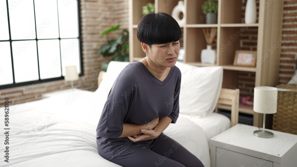Young chinese woman suffering for menstrual pain sitting on bed at bedroom Young chinese woman suffering for menstrual pain sitting on bed at bedroom