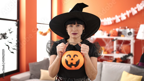 Young chinese woman wearing witch costume holding halloween pumpkin basket at home
