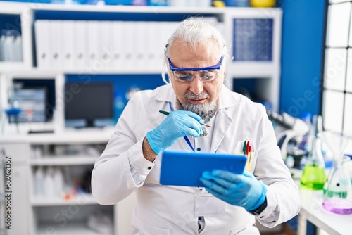 Middle age grey-haired man scientist using touchpad at laboratory