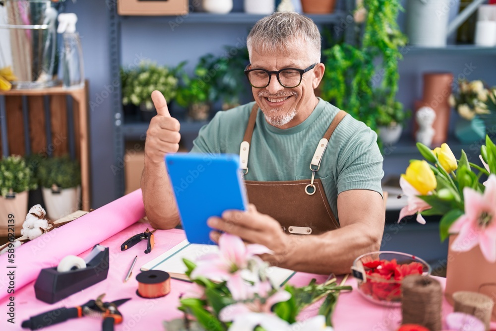 Hispanic man with grey hair working at florist shop doing video call with tablet smiling happy and positive, thumb up doing excellent and approval sign Hispanic man with grey hair working at florist shop doing video call with tablet smiling happy and positive, thumb up doing excellent and approval sign