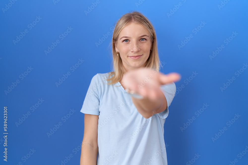 Young caucasian woman wearing casual blue t shirt smiling cheerful offering palm hand giving assistance and acceptance.