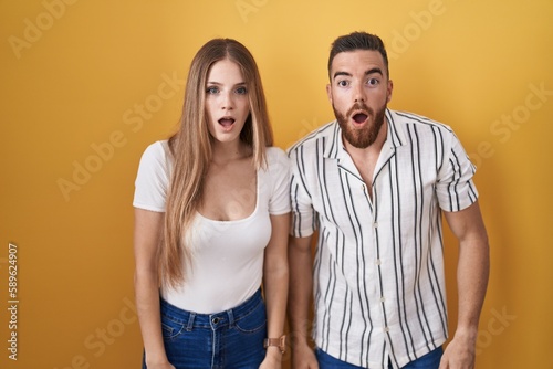 Young couple standing over yellow background afraid and shocked with surprise and amazed expression, fear and excited face.