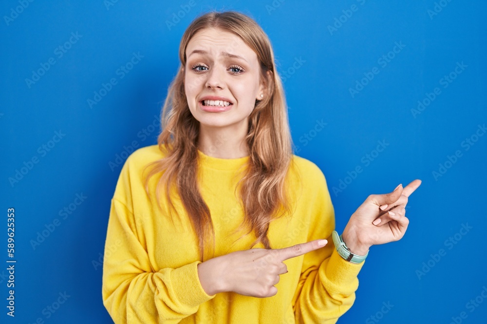 Young caucasian woman standing over blue background pointing aside worried and nervous with both hands, concerned and surprised expression Young caucasian woman standing over blue background pointing aside worried and nervous with both hands, concerned and surprised expression