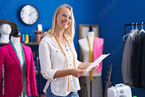 Young blonde woman tailor smiling confident reading paper at sewing studio photo