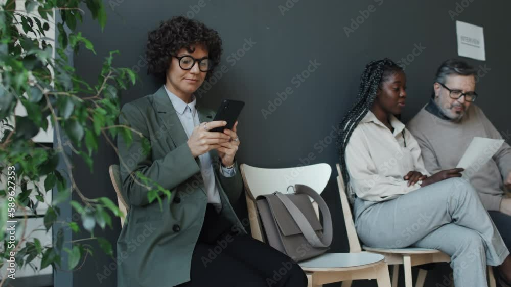 Medium shot of Caucasian woman using her smartphone then looking to side while black woman talking to Caucasian man in background Medium shot of Caucasian woman using her smartphone then looking to side while black woman talking to Caucasian man in background
