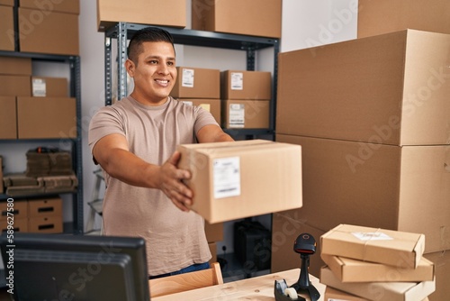 Young latin man ecommerce business worker holding package at office