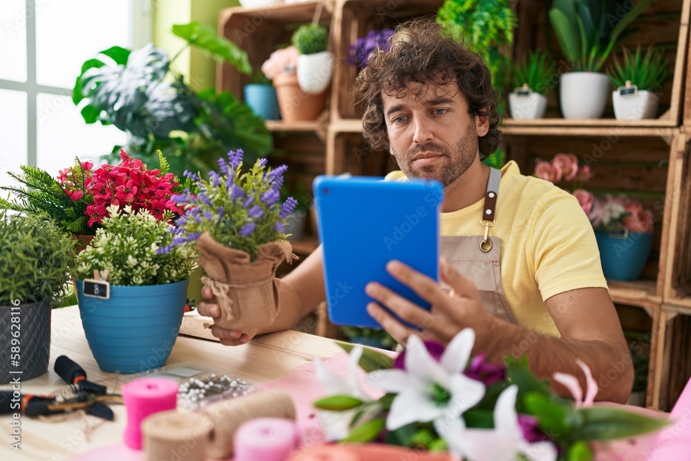 Young hispanic man florist using touchpad holding lavender plant at flower shop