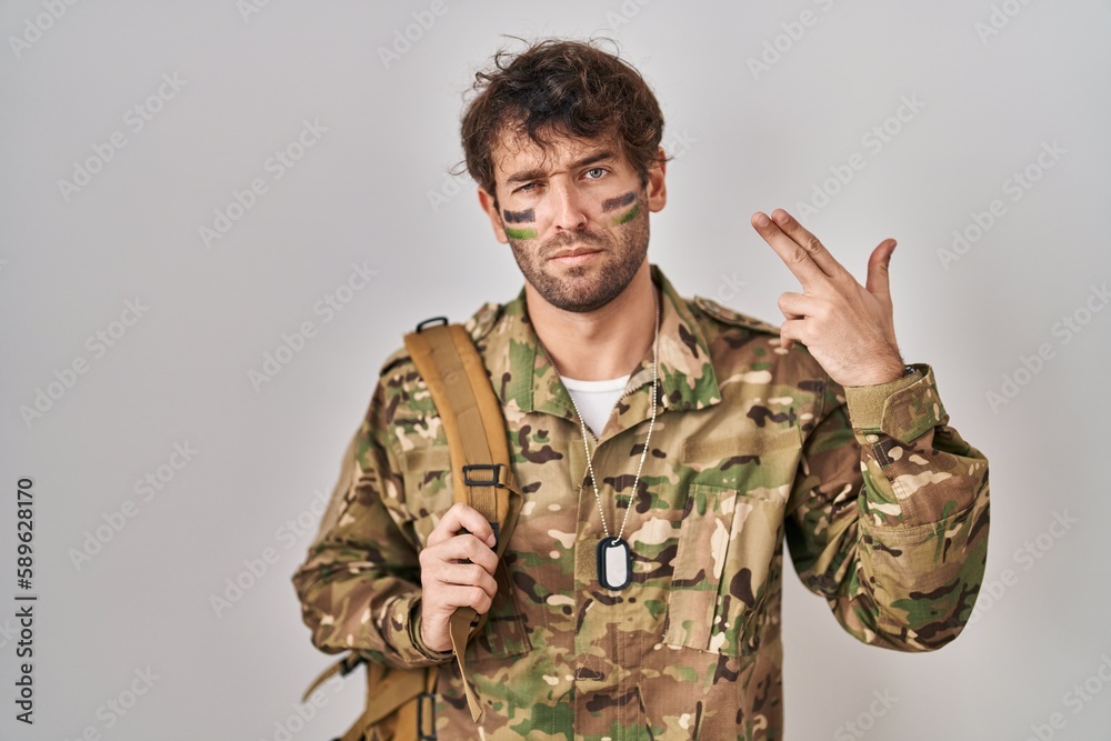 Hispanic young man wearing camouflage army uniform shooting and killing oneself pointing hand and fingers to head like gun, suicide gesture.