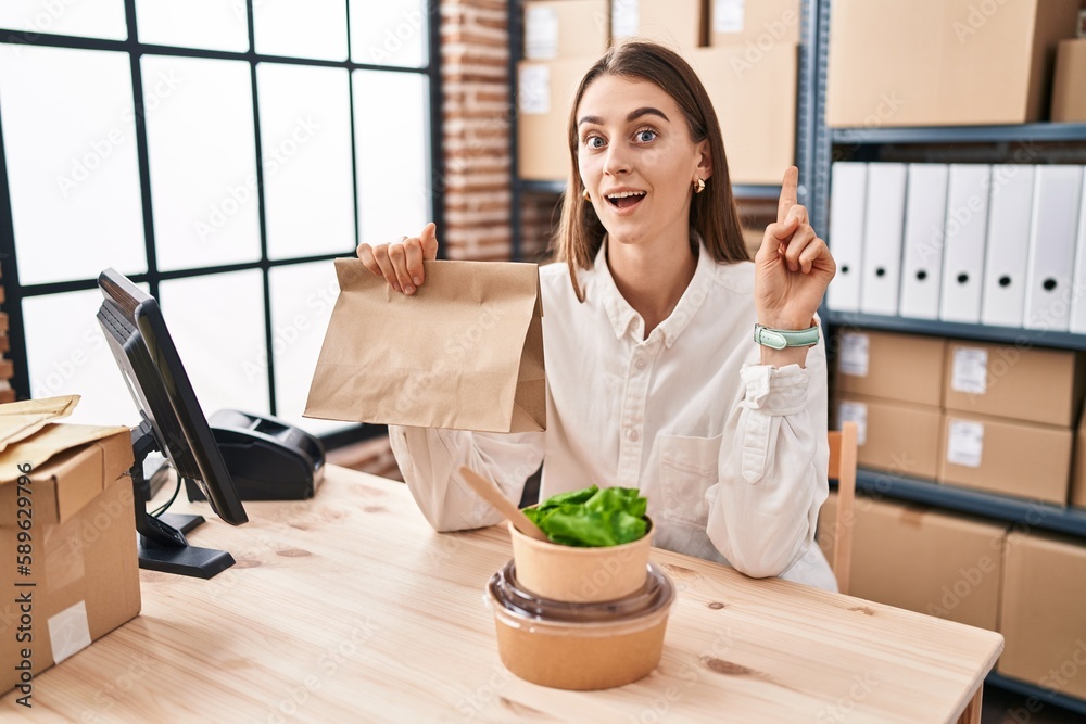 Young caucasian woman working at small business ecommerce holding take away food surprised with an idea or question pointing finger with happy face, number one