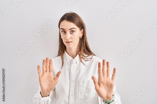 Young caucasian woman standing over isolated background moving away hands palms showing refusal and denial with afraid and disgusting expression. stop and forbidden.