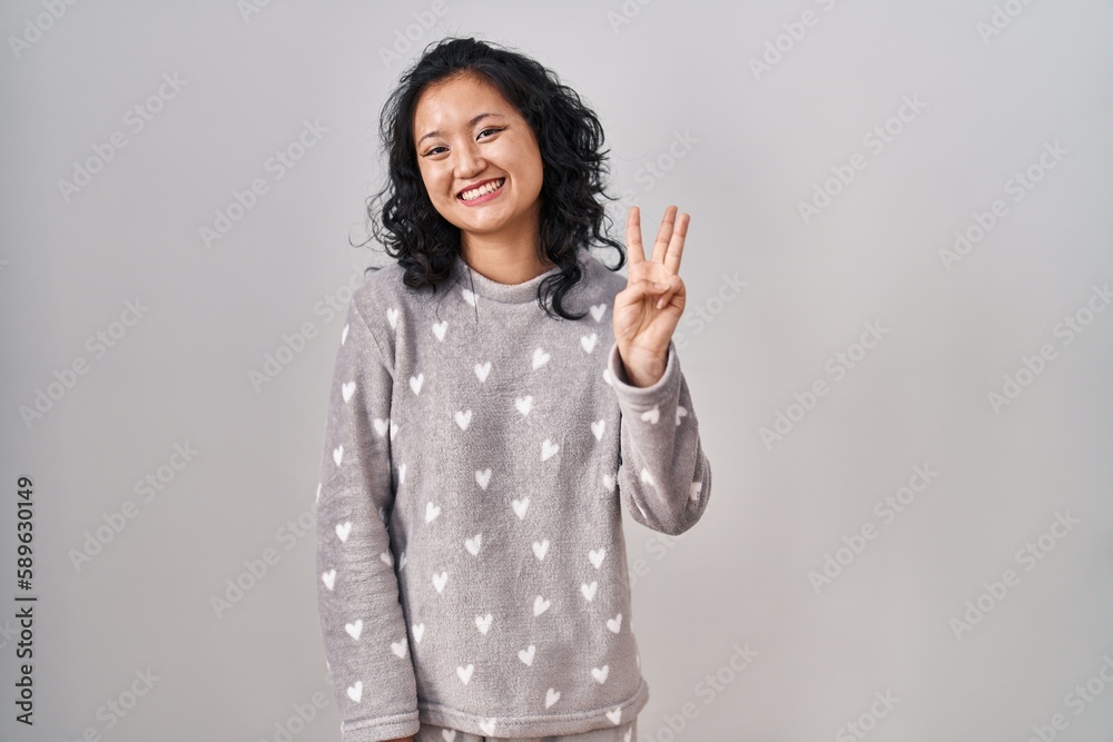 Young asian woman wearing pajama showing and pointing up with fingers number three while smiling confident and happy. Young asian woman wearing pajama showing and pointing up with fingers number three while smiling confident and happy.