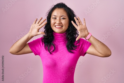 Young asian woman standing over pink background showing and pointing up with fingers number ten while smiling confident and happy.
