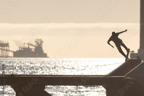 Young skateboarder trains on the waterfront on the ramp at early sunset photo