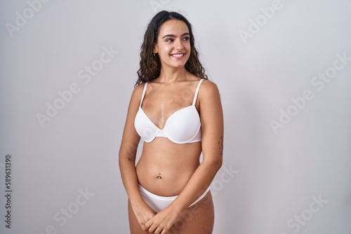 Young hispanic woman wearing white lingerie looking away to side with smile on face, natural expression. laughing confident.