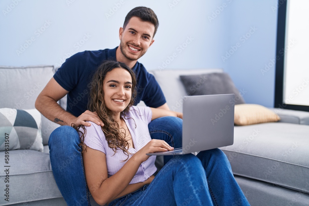 Young hispanic couple using laptop sitting on sofa at home