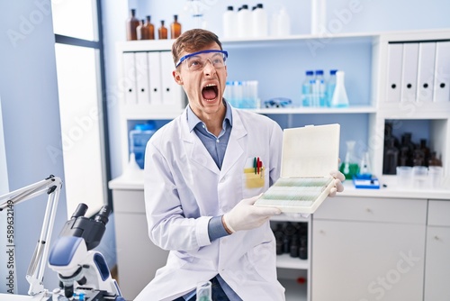 Caucasian man working at scientist laboratory angry and mad screaming frustrated and furious, shouting with anger looking up.