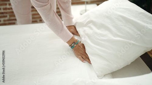 Middle age hispanic woman make bed at bedroom