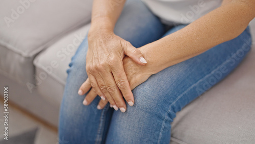 Middle age hispanic woman sitting on sofa with hands on knees at home