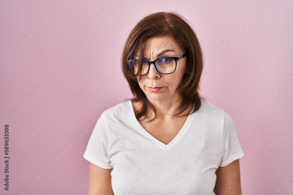 Middle age hispanic woman standing over pink background skeptic and nervous, frowning upset because of problem. negative person. Middle age hispanic woman standing over pink background skeptic and nervous, frowning upset because of problem. negative person.