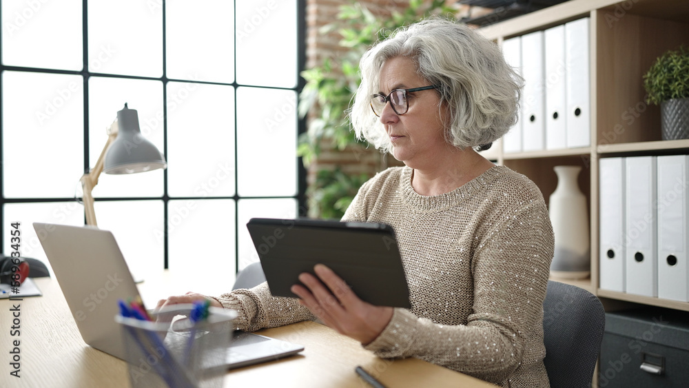 Middle age woman with grey hair business worker using touchpad and laptop at office Middle age woman with grey hair business worker using touchpad and laptop at office