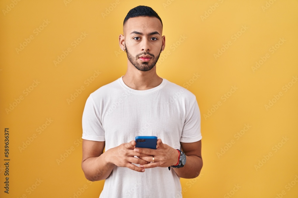 Young hispanic man using smartphone typing message relaxed with serious expression on face. simple and natural looking at the camera. Young hispanic man using smartphone typing message relaxed with serious expression on face. simple and natural looking at the camera.