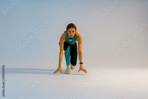 Sporty woman in starting position ready for running looking at camera on studio background