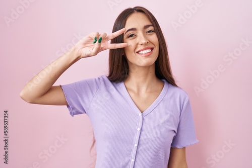 Wallpaper Mural Young hispanic woman with long hair standing over pink background doing peace symbol with fingers over face, smiling cheerful showing victory Torontodigital.ca