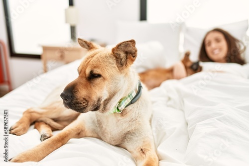 Young hispanic woman hugging dog lying on bed at bedroom