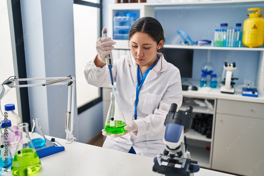 Young hispanic woman wearing scientist uniform using pipette working at laboratory Young hispanic woman wearing scientist uniform using pipette working at laboratory