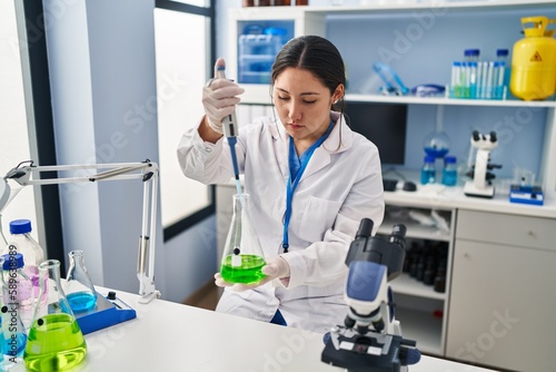 Young hispanic woman wearing scientist uniform using pipette working at laboratory