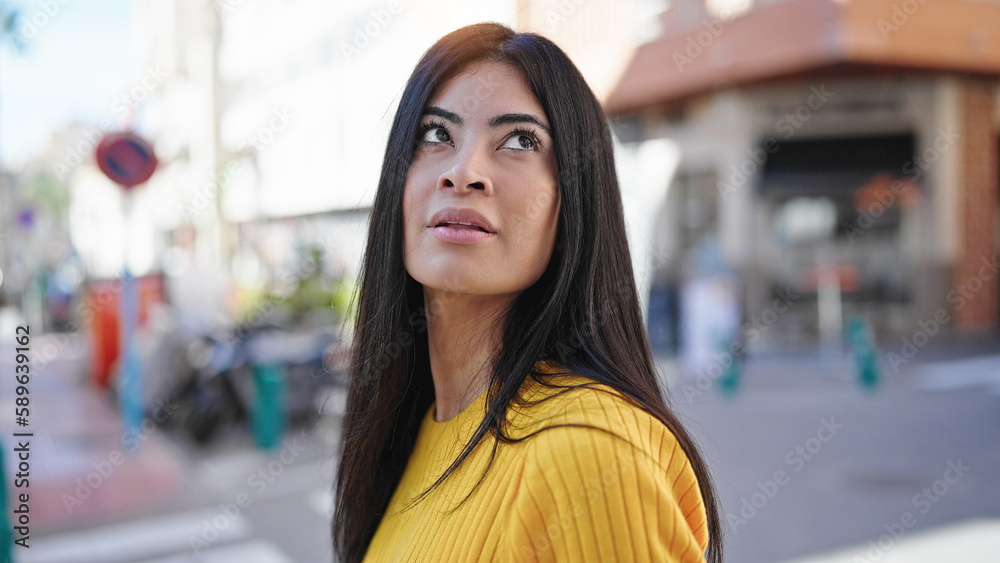 Young beautiful hispanic woman looking to the sky with serious expression at street Young beautiful hispanic woman looking to the sky with serious expression at street