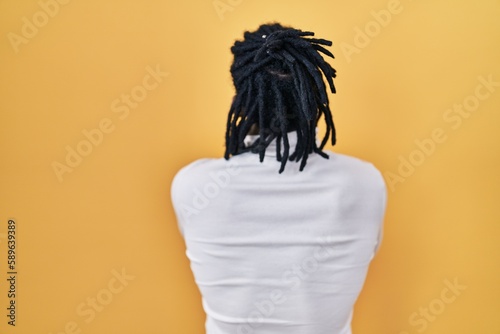 African man with dreadlocks wearing turtleneck sweater over yellow background standing backwards looking away with crossed arms photo