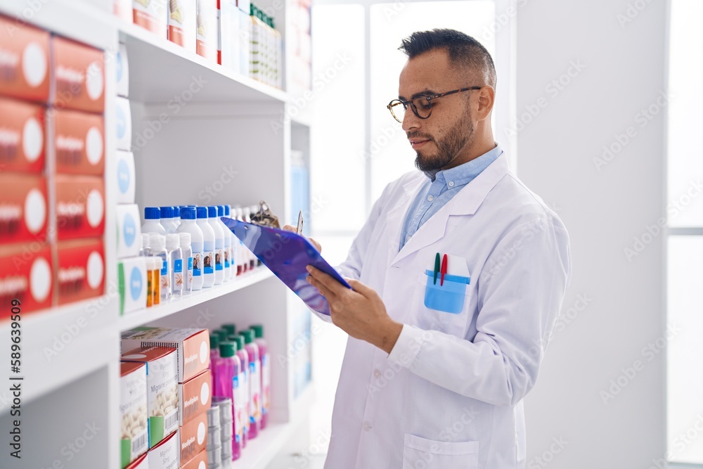 Young hispanic man pharmacist writing on document at pharmacy