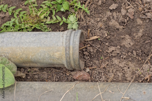 one gray metal sewer pipe lies on brown earth among green vegetation on the street