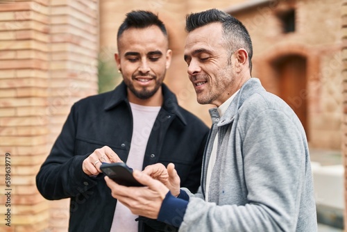 Two men couple smiling confident using smartphone at street